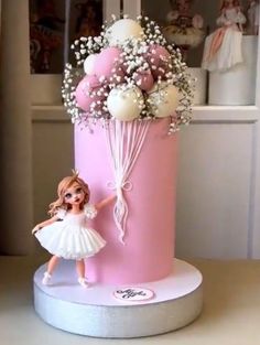 there is a pink cake with a doll on it and flowers in the top tier