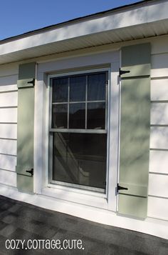 a white house with green shutters and a cat sitting on the window sill