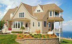 a large house sitting on top of a lush green field next to the ocean with lots of windows