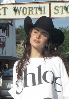 a woman wearing a black cowboy hat standing in front of a store with her hand on her hip