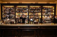 a man behind the bar at a restaurant with lots of liquor bottles on shelves above it