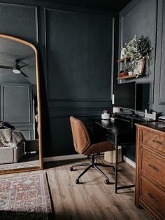 a desk with a chair and mirror in a room that has dark walls, wood floors and wooden furniture