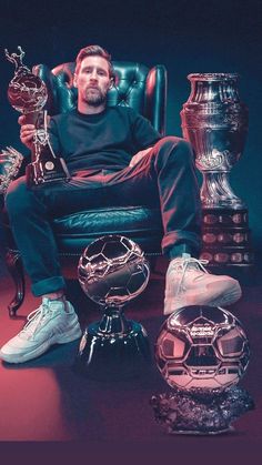 a man sitting in a chair with trophies and soccer balls on the floor next to him