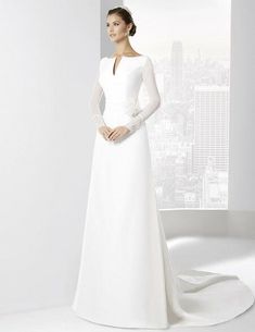 a woman in a white wedding dress standing next to a window with the city skyline behind her