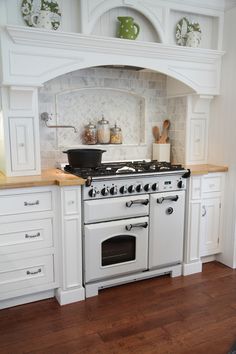 a white stove top oven sitting inside of a kitchen next to wooden flooring and cabinets