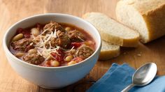 a white bowl filled with meat and bean soup next to sliced bread on a wooden table