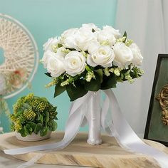 a bouquet of white roses sits on a table next to a small potted plant