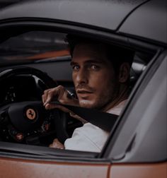 a man sitting in the driver's seat of a sports car with his hand on the steering wheel