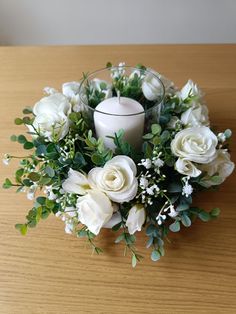 a candle and some white flowers on a wooden table with greenery around the edges