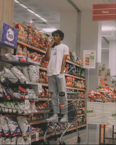 a man standing on top of a shopping cart talking on a cell phone in a grocery store