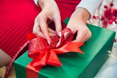 a woman's hands holding a green gift box with red ribbon and bow on it