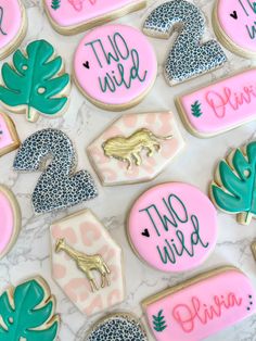 decorated cookies with pink and green frosting on a marble surface, including palm leaves