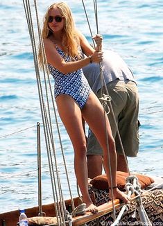 a woman in a blue and white swimsuit standing on the bow of a boat