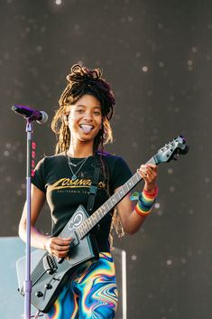 a woman with dreadlocks holding a guitar and singing into a microphone on stage