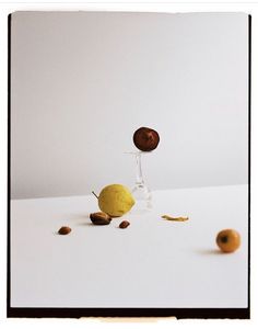 an apple and two oranges on a white surface with one falling into the air