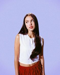 a woman with long dark hair wearing a white shirt and red skirt standing in front of a blue background