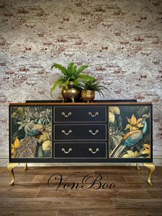 an old dresser with birds painted on it and plants in the top drawer, against a brick wall