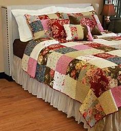 a bed with a colorful quilt on top of it next to a lamp and window