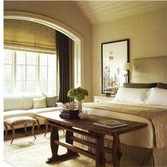 a large bed sitting next to a wooden table in a room with white walls and windows