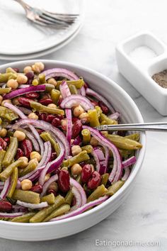 a bowl filled with beans, onions and green beans on top of a white table