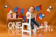 a little boy sitting on a chair in front of a birthday sign and decorations for his first birthday