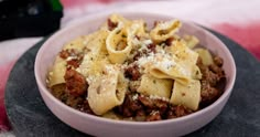 a bowl filled with pasta and meat on top of a table next to a bottle