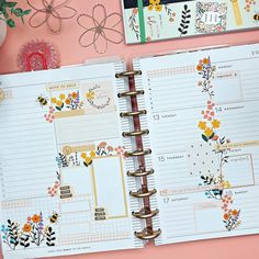 an open planner book sitting on top of a pink table next to flowers and other items