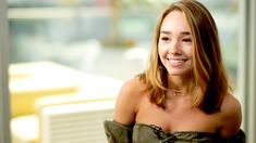 a smiling woman in off the shoulder top sitting at a table next to a window