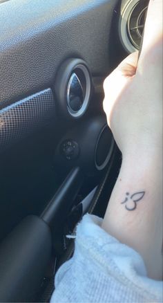 a person with a small tattoo on their left arm in a car, holding the steering wheel