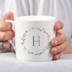 a person holding a coffee mug with the letter h on it's front and side