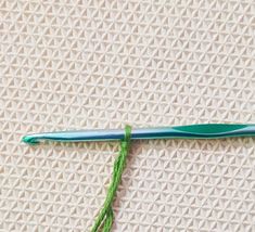 a crochet hook with green thread on it and a blue needle in the middle