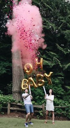 two people standing in front of a tree with pink and gold balloons