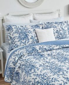 a bed with blue and white comforters in a bedroom next to a mirror on the wall