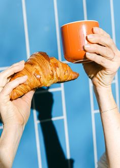 a person holding a coffee cup and croissant in their hands