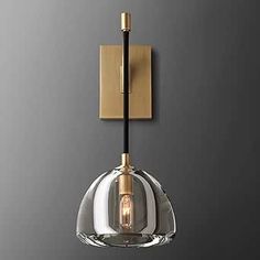 a glass light fixture hanging from the side of a gray wall with a gold finish