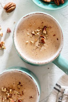 two mugs filled with milk and nuts on top of a white tablecloth next to a bowl of pecans