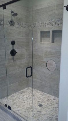 a walk in shower sitting next to a white wall and tiled floor with black handles