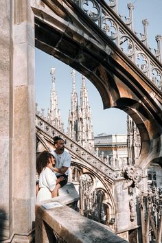 a man and woman sitting on top of a stone wall next to each other in front of a cathedral