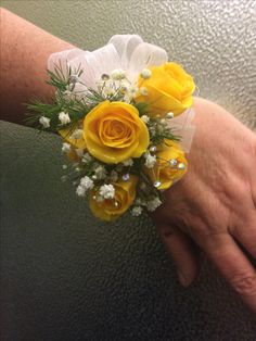 a person's hand holding a yellow and white wrist corsage