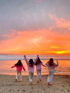 three girls are running on the beach with their arms in the air as the sun sets