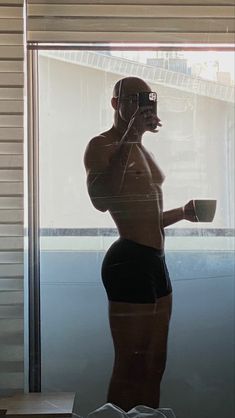 a reflection of a man in a window holding a coffee cup and cell phone to his ear