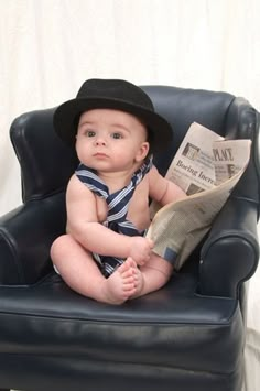 a baby sitting in a chair with a newspaper on it's lap and wearing a hat