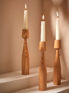 three wooden candlesticks sitting on top of a shelf next to another candle holder