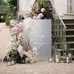 a wedding sign with flowers and candles on the ground next to some stairs in front of a building