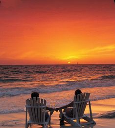 two people sitting in chairs on the beach at sunset