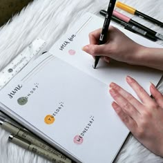 a person's hand holding a pen and writing on top of a notebook with various markers