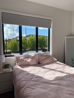 a bed with pink sheets and pillows in front of a large window that looks out onto the mountains