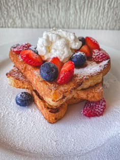 french toast topped with berries, whipped cream and powdered sugar on a white plate