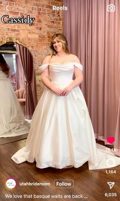 a woman standing in front of a mirror wearing a white wedding dress with off the shoulder sleeves