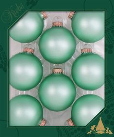 six green christmas balls in a box with gold trimmings on the top and bottom